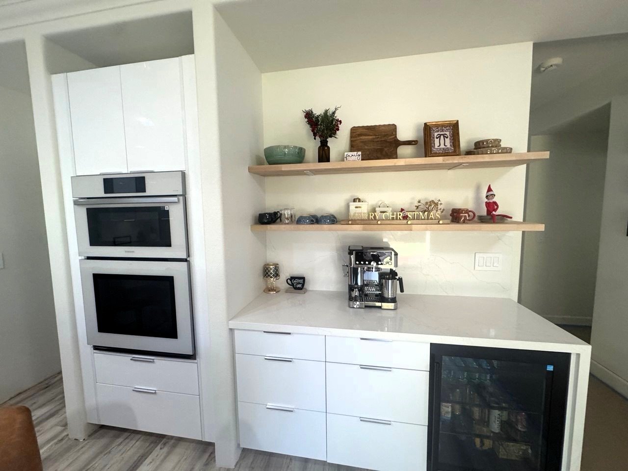 White gloss cabinetry with a wall oven tower, floating shelves, a coffee bar and a beverage fridge, an Island Contractors remodel